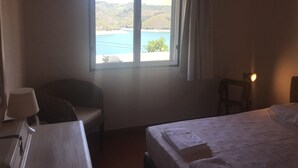A bedroom with a bed, a chair, a desk, and a window offering a view of a beach and hills. - House in Castelo de Bode, blue lake (Castelo de Bode)