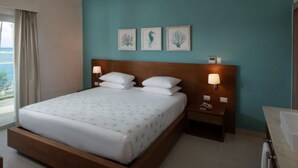 Une chambre d’hôtel avec un grand lit, deux tables de chevet avec des lampes et trois reproductions encadrées de motifs botaniques accrochées au mur.