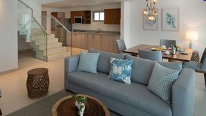 Un salon moderne avec un canapé gris, une table basse et un escalier menant à la cuisine.