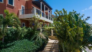 A multi-story building with a balcony, surrounded by lush greenery and palm trees.