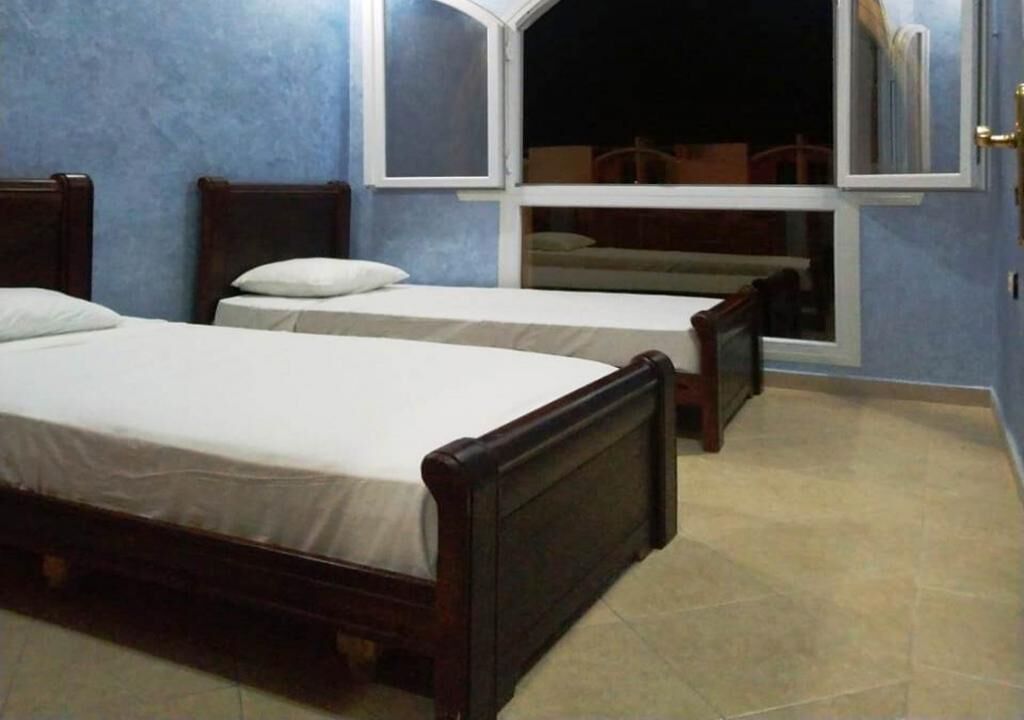 Una habitación con dos camas de madera, un ventanal con vistas y suelo de baldosas.
