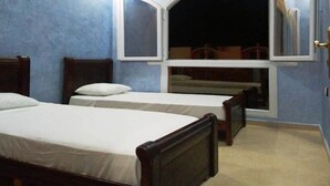 Una habitación con dos camas de madera, un ventanal con vistas y suelo de baldosas.