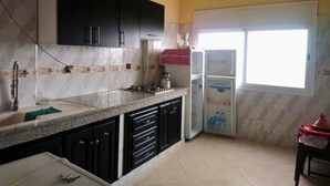 Una cocina con armarios oscuros, protector contra salpicaduras de mármol, un lavabo, una estufa y un refrigerador.