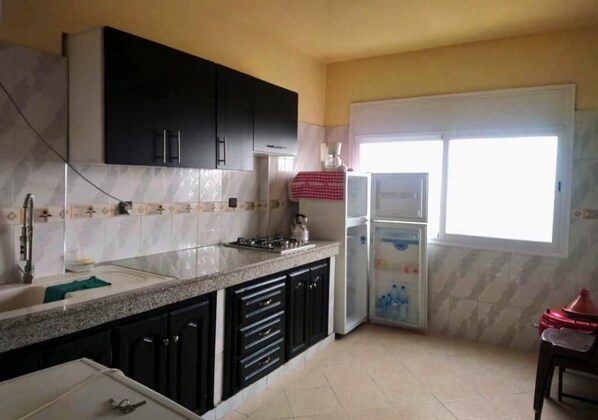 A kitchen with dark cabinets, a marble backsplash, a sink, a stove, and a refrigerator.