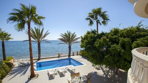 Une piscine avec des chaises longues et des tables, des palmiers et une vue sur la mer.