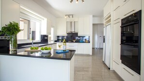 Une cuisine moderne avec des meubles blancs, un îlot central, une hotte en acier inoxydable et des appareils électroménagers intégrés.