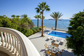 A poolside area with a view of the sea, palm trees, and a dining setup. - Meneou Sunset Beachfront Villa (Larnaca)