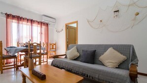 Una sala de estar con un sofá, dos sillones, una mesa de madera y una mesa de comedor con sillas.