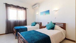 Una habitación con dos camas individuales, una ventana con cortinas, un equipo de aire acondicionado y un cuadro en la pared.