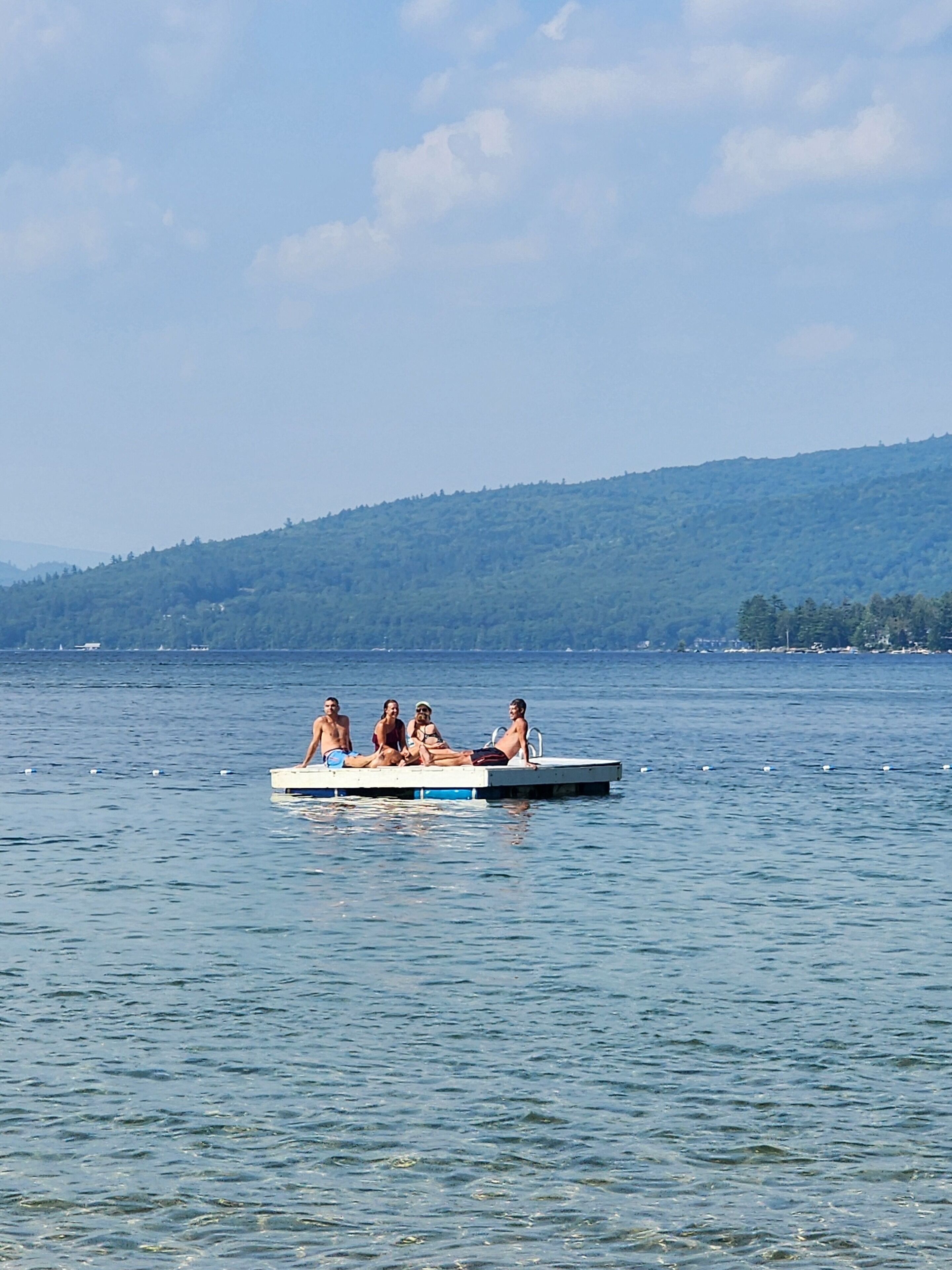 A group of people on a small boat on a lake with a forested hill in the background.