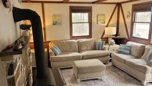 Ein gemütliches Wohnzimmer mit Kamin aus Stein, einem beigen Ecksofa und einer Holzzahlendecke.