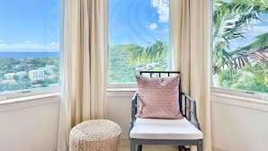 A room with a view of a coastal landscape, a chair with a cushion, and a woven stool. - Frangipani Private Pool and Tesla Backup! (St. John)