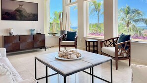 A spacious room with a large window offering a view of the ocean and palm trees, a wooden ceiling, and a dining area with a table set for two. - Frangipani Private Pool and Tesla Backup! (St. John)