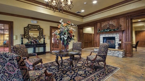 A formal room with a fireplace, patterned chairs, a central table with a vase of flowers, and a chandelier. - Branson Condo at Pointe Royale with Indoor Pool and Hot Tub on Taneycomo Lake ne (Branson)