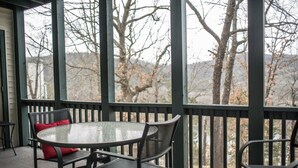 A covered outdoor seating area with a round table and chairs, a red cushion, and a view of leafless trees and hills. - Branson Condo at Pointe Royale with Indoor Pool and Hot Tub on Taneycomo Lake ne (Branson)