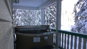 Un bain à remous avec un banc en bois et un panneau d’avertissement, le tout installé sur un fond enneigé, avec une clôture en bois en arrière-plan.