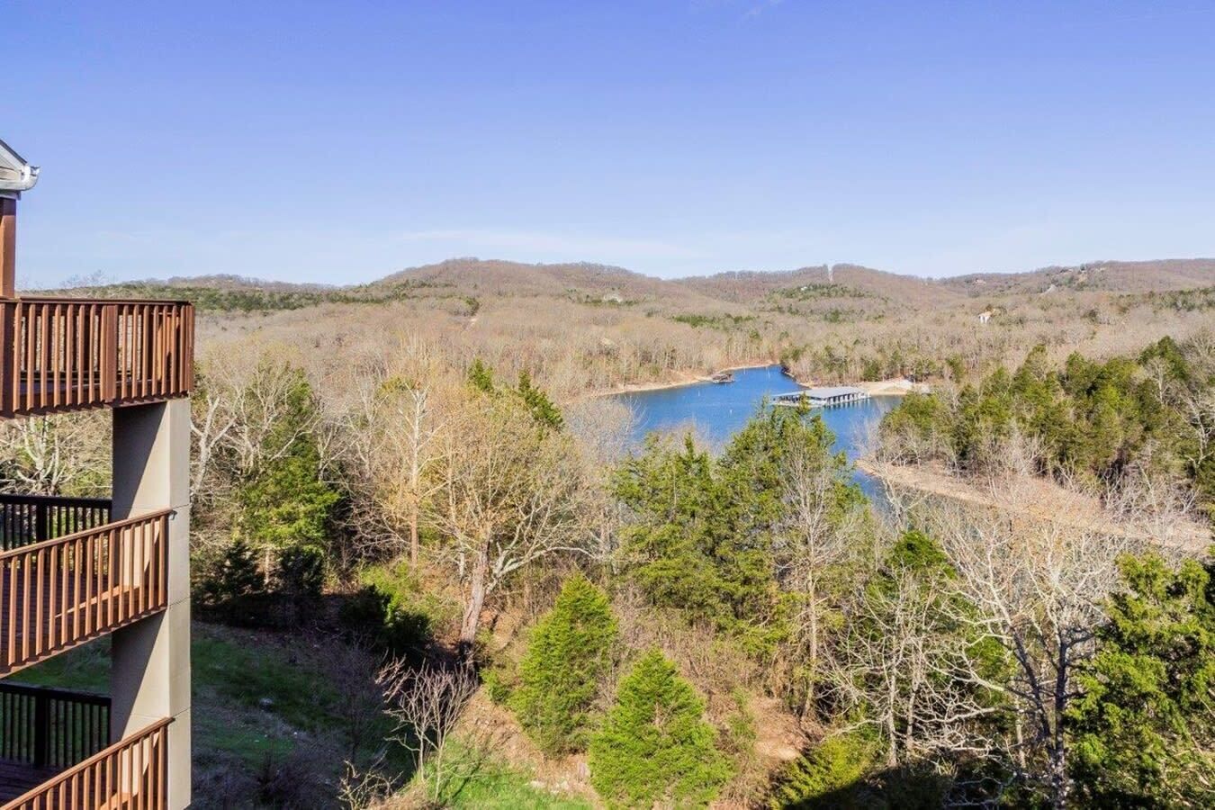 A view of a building with a balcony overlooking a natural landscape with a body of water and trees.