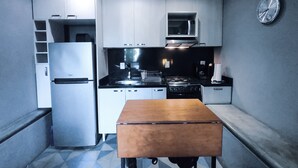 Cocina compacta con refrigerador, estufa, microondas y un banco de madera.