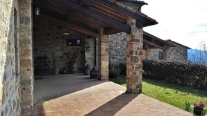 Ein Steinhaus mit überdachter Terrasse, Steinpfeilern und einem Pflasterboden.