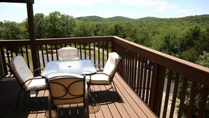 Une terrasse en bois avec une table et quatre chaises, donnant sur une zone boisée.