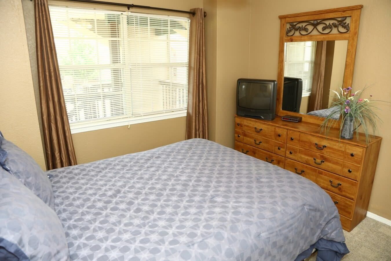 A bedroom with a bed, a dresser, a television, and a mirror.