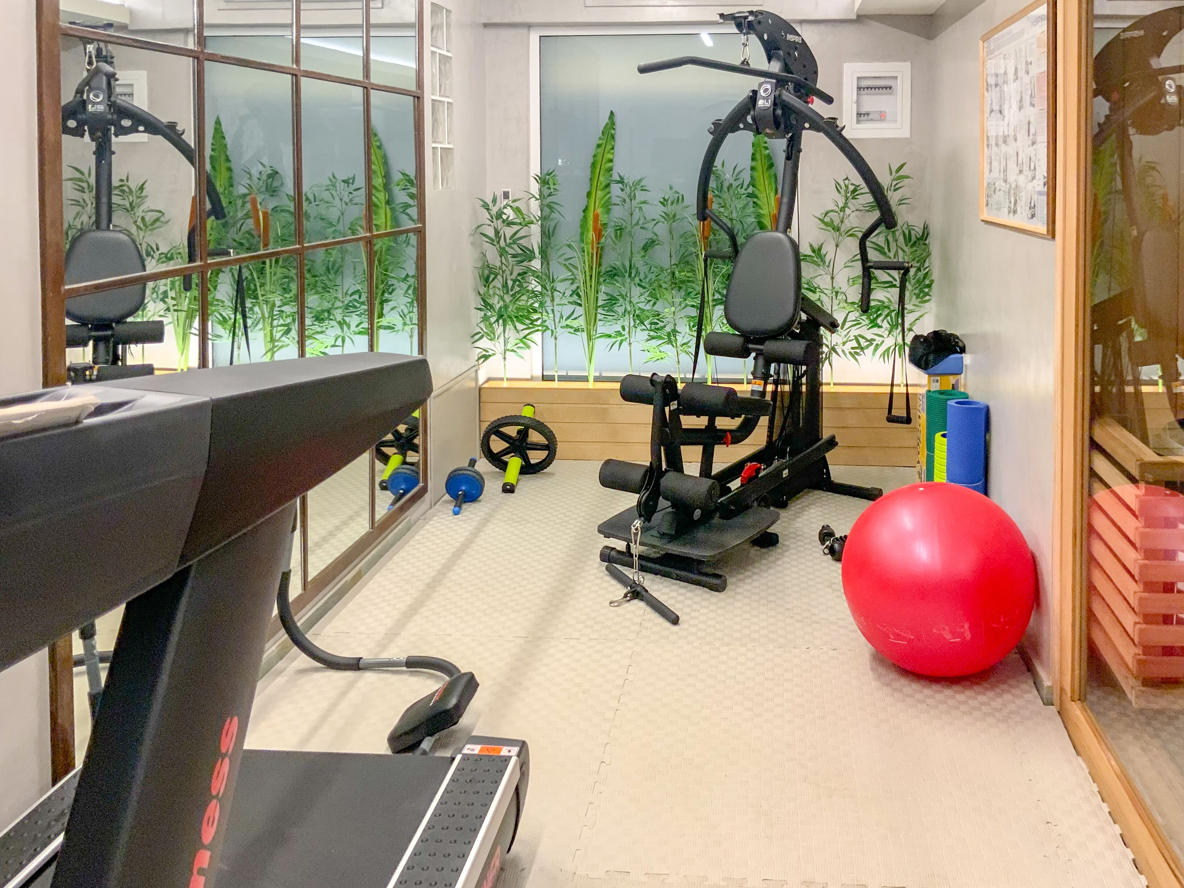 Une salle de sport équipée de matériel d’exercice, d’un tapis de course et d’un ballon rouge.