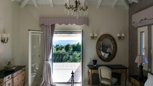 Een slaapkamer met een bed, een bureau, een stoel, een dressoir, een kroonluchter, een spiegel en een balkon met uitzicht.