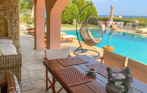 Un espace aménagé au bord de la piscine, avec des meubles en osier, un fauteuil suspendu et une vue sur la mer.