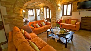 A cozy living room with orange sofas, a coffee table with fruits and a vase, a TV, and a fireplace. - Villa Serena - Homelike Villas (Sant'Angelo in Pontano)