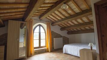 Une chambre avec un plafond en pente, une grande fenêtre en arc de cercle, un lit, une table de chevet et un radiateur.