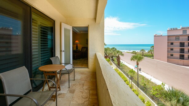 A balcony with a table and chairs, a view of the beach, and a building in the background. - Condo with Gulf View just steps to our private Siesta Key Beach! (Sarasota)