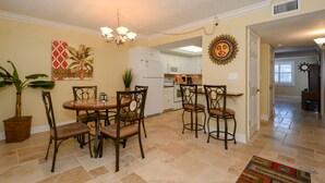 A dining area with a round table and four chairs, a chandelier, a potted plant, and a painting on the wall. - Condo with Gulf View just steps to our private Siesta Key Beach! (Sarasota)