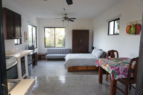 Un dormitorio con cama, mesita de noche, ventana y ventilador de techo.