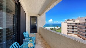 A balcony with a view of the beach, a table with chairs, and a door.