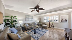 A spacious living room with a ceiling fan, large windows, and a view of the outdoors.