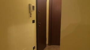 A narrow hallway with a door at the end, a wall socket, and a light switch. - Asti historic center cathedral (Asti)
