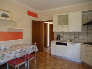 Cocina compacta con armarios blancos, cafetera y una mesa de comedor con sillas.