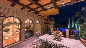 An outdoor patio with a brick wall, arched windows, and a table with chairs. - Fontespina 6, Emma Villas (Conca degli Ulivi)