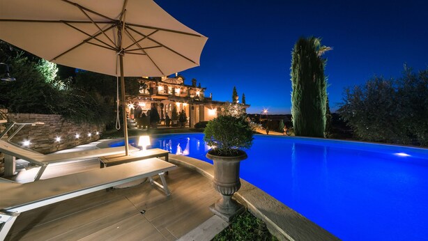 A swimming pool with a patio area, a large umbrella, and a well-lit building in the background. - Fontespina 6, Emma Villas (Conca degli Ulivi)
