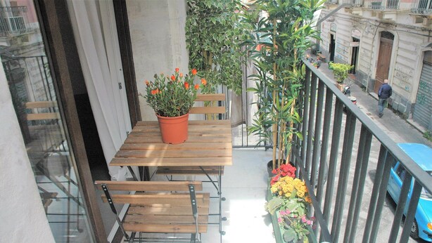 A balcony with a wooden table and chairs, a potted plant with orange flowers, and a railing. - The sunny House "In the center"  (Catania)