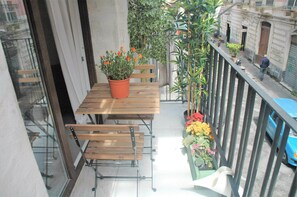 Un balcon avec une table et des chaises en bois, un pot de fleurs orné de fleurs oranges et une rambarde.