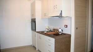 A compact kitchen with white cabinets, a built-in oven, a sink, and a countertop with a kettle and utensils. - The sunny House "In the center"  (Catania)