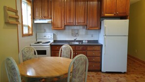 A kitchen with wooden cabinets, a white stove, a refrigerator, and a dining table with chairs.