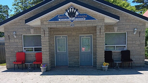 A stone building with a sign for Suites of Wasaga, featuring two doors, a small patio area with chairs, and a stone facade.