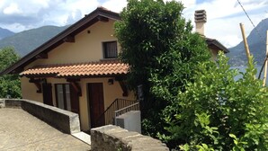 Une maison traditionnelle en pierre, avec un toit en tuiles, un escalier en bois et une vue sur les montagnes en arrière-plan.