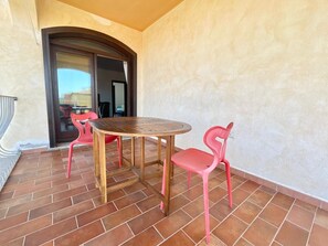 A patio with a round wooden table and two pink chairs, a tiled floor, and a door leading to an interior space. - Elegant apartment with sea view at La Maddalena (La Maddalena)