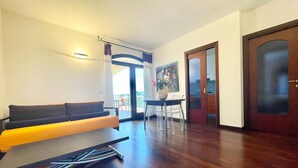 A living room with a sofa, a dining table with chairs, and a door. - Elegant apartment with sea view at La Maddalena (La Maddalena)