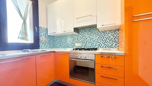 A kitchen with orange cabinets, a tiled backsplash, a window with curtains, and a stove. - Elegant apartment with sea view at La Maddalena (La Maddalena)