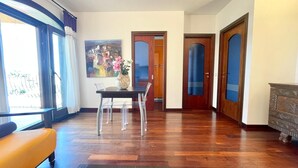 A spacious living room with a wooden floor, a dining table with chairs, a sofa, and a painting on the wall. - Elegant apartment with sea view at La Maddalena (La Maddalena)