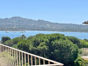 A balcony with a view of a coastal landscape, including a body of water and distant hills.